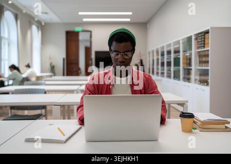African American student hipster guy or intern using laptop studying, passes virtual training, preparing to exams at university lecture classroom. Bus Stock Photo