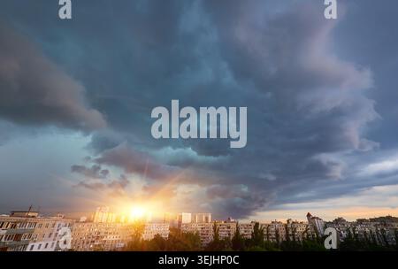 Dark, heavy storm clouds gather over a city skyline, with breaks of sunlight illuminating parts of the dramatic sky. Impending rain or clearing storm. Stock Photo