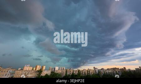 Dark, heavy storm clouds gather over a city skyline, with breaks of sunlight illuminating parts of the dramatic sky. Impending rain or clearing storm. Stock Photo