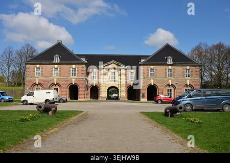 Symmetrical historic brick building with central arch, cannons and parked vehicles outside Stock Photo