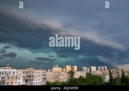 Dark, heavy storm clouds gather over a city skyline, with breaks of sunlight illuminating parts of the dramatic sky. Impending rain or clearing storm. Stock Photo