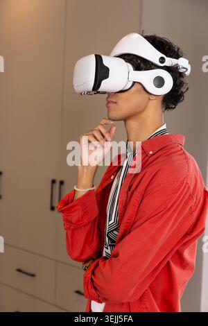 Male wearing white VR headset with integrated headphones and red overshirt, standing near cabinets. Technology, innovation, immersive, modern, leisure Stock Photo