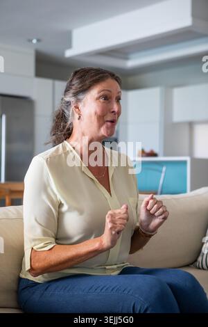 Woman sitting on a beige sofa in an open-plan living area, engaged in lively conversation, with a fruit bowl next to her. Modern Stock Photo