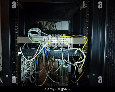 disorganized server rack network switches and patch panels, numerous Ethernet cables connected to the devices, showing a high density of connections. Stock Photo