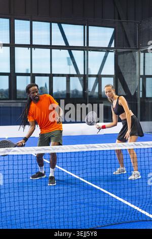 Various athletes with padel rackets leaning against the net on a covered padel court. Dynamic, teamwork, athleticism, modern, co Stock Photo