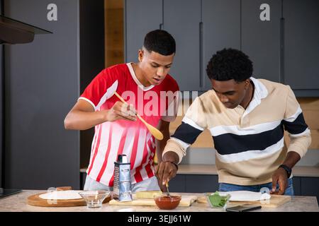 Various male friends prepare pizza dough on a kitchen island using a rotating cheese grater and a spoon. Cooking, culinary arts, Stock Photo