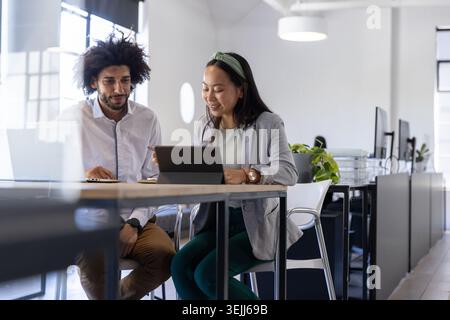Diverse employees working together on tablets and notebooks at a standing table in a modern office. Desk, collaboration, busines Stock Photo