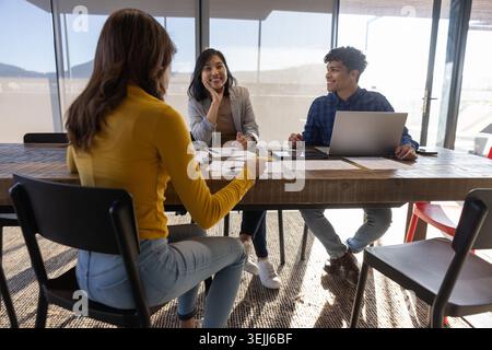Diverse employees in business casual attire discuss strategy in a conference room at a wooden table. Collaboration, professional Stock Photo