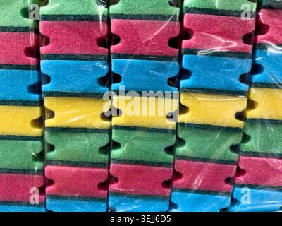 Close-up of new colorful multi-colored kitchen dishwashing sponges stacked in rows inside a transparent plastic package. Stock Photo