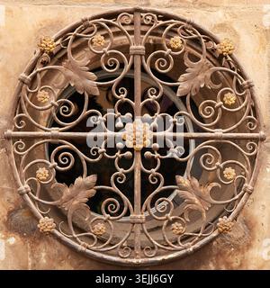 Ornate circular wrought iron window grille with elegant floral and swirl patterns on an old stone building facade. Stock Photo