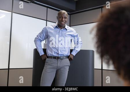 Various employees stand on a podium and talk to a colleague in an office with frosted glass walls. Professional, presentation, c Stock Photo