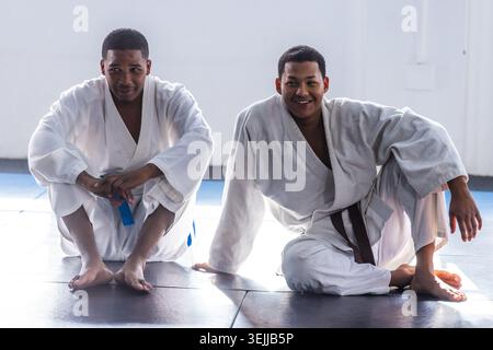 African American training partners sitting on mats in martial arts gym wearing white gis and belts. Martial arts, training, fitn Stock Photo