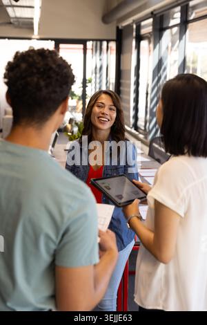 Diverse coworkers collaborating around printed documents and using tablet at open-plan office desk. Collaboration, teamwork, inn Stock Photo