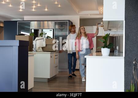 Couple in their thirties inspecting kitchen cabinetry and gesturing toward moving boxes on island. Modern, minimalist, lifestyle, interior, design, ho Stock Photo