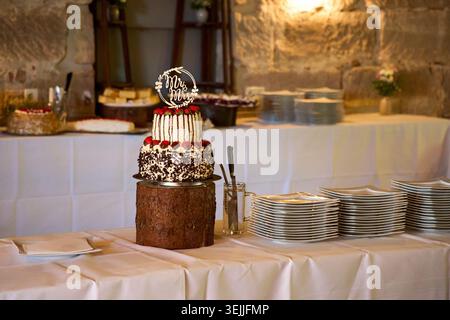 Multi-tiered wedding cake with a "Mr & Mrs" topper on a wooden stump stand at a reception buffet. Stock Photo