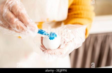 Close up of woman hands in gloves coloring easter eggs Stock Photo