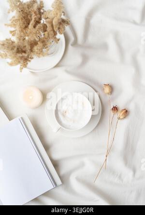 White blank book with cup of coffee and burning candle , cozy composition with opened book mockup Stock Photo