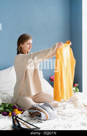 Young woman organizing clothes sitting on the bed at home Stock Photo