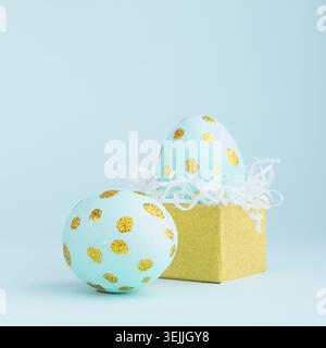 Elegant easter eggs with gold dots and golden gift box on blue background, square. Stock Photo