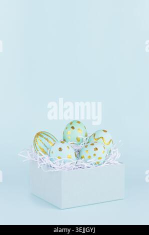 Simple and minimal easter background - easter eggs with golden design in gift box on blue color, vertical. Stock Photo