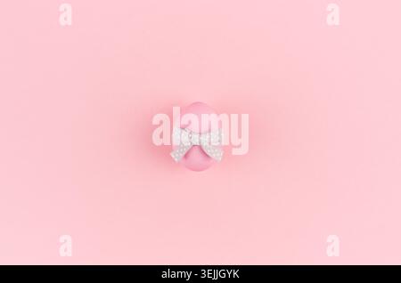 Pink easter egg with grey ribbon standing on pastel pink background, copy space. Stock Photo