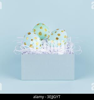 Blue easter eggs with gold glitter dots in gift box on blue background, square. Stock Photo