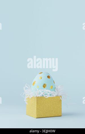 Fashion easter background - blue egg with golden dots in golden gift box on blue color, vertical. Stock Photo