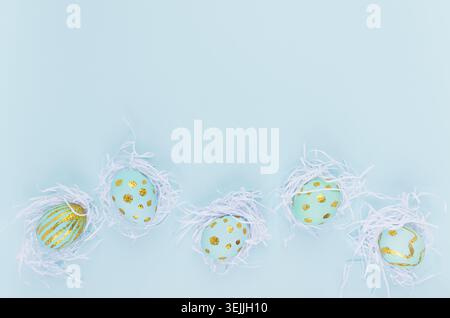 Stylish easter background - blue easter eggs with gold design in white nest as border on blue color, top view. Stock Photo