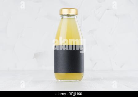 Yellow pineapple juice in glass bottle with gold cap and black blank label mock up on white wood table in light interior with co Stock Photo