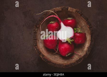 Fresh radishes displayed in a wooden bowl on a rustic surface for a wholesome culinary experience Stock Photo
