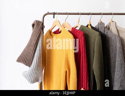 Row of different colorful Knitted sweaters hang on hangers, white background Stock Photo