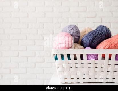 Pastel colored yarn wool in a white basket on white brick wall background Stock Photo
