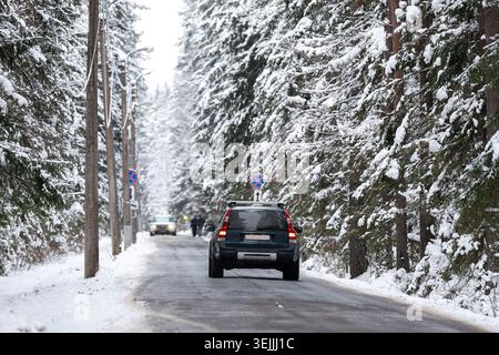 Car driving on frosty countryside road through spruce forest covered in snow on cold winter day. Stock Photo