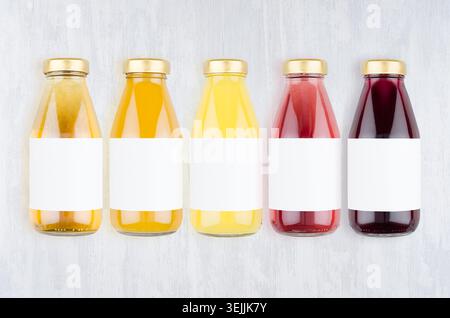 Organic fruits juices - set of different color juices with cap in glass bottles with blank label on white wood background, mock Stock Photo