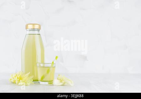 Fresh vegetable green celery juice in glass bottle mock up with glass, straw, stems in soft light white interior on wood table. Stock Photo