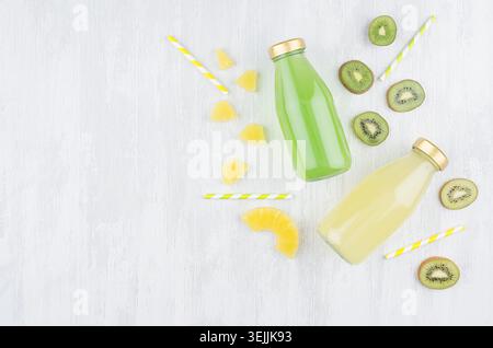 Fresh yellow pineapple and green kiwi juices in glass bottles with sliced fruit, straws on white wooden board, top view, copy sp Stock Photo
