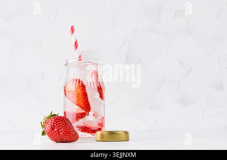 Summer homemade drink - infused strawberry water with sliced berry, ice cubes, soda, cap, straw in soft light white interior, co Stock Photo