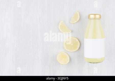 Organic lemon yellow juice in glass bottle with blank label, sliced citrus on white wood background, top view, copy space, mock Stock Photo
