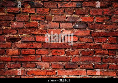 Red brick wall displaying cracked surfaces and worn mortar, creating a gritty texture Stock Photo