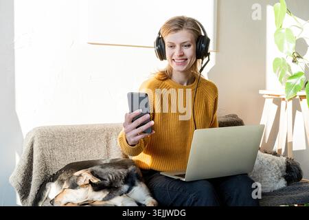 Young smiling woman in black headphones studying online using laptop Stock Photo