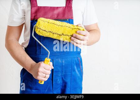 Closeup of a worker in blue overalls with a roller for coloring walls Stock Photo