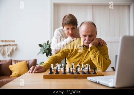 Senior old man playing chess game on chess board, online game with friend, video call due to social distancing at home. Senior c Stock Photo
