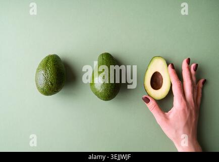 Woman hand holding a half of avocado on the green background top view Stock Photo
