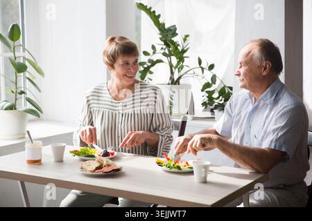 Portrait of relaxed fun senior couple together and eating breakfast in their kitchen at home Stock Photo