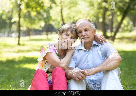 Happy Elderly Senior couple sitting on grass together relaxing in the garden. Stock Photo