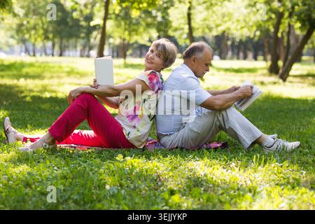 Senior couple read books lying on the grass in the park Stock Photo