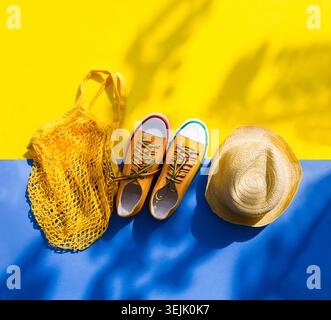 Mesh shopping bag with bananas, straw hat and  Yellow sneakers  flowers dandelions on yellow background with shadows of trees. E Stock Photo