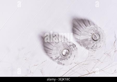 Elegant fracile lifestyle background with dry grass straws, transparent bottles in sunlight, shadows on white wood board, top vi Stock Photo