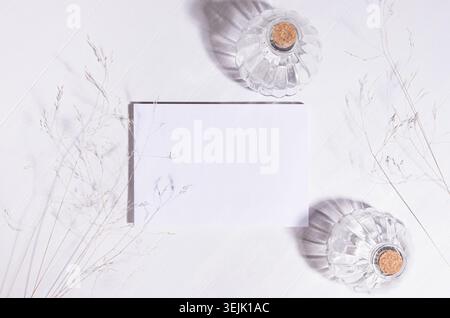 Elegant fracile lifestyle background with blank paper for portfolio, dry grass straws, bottles in sunlight, shadows on white woo Stock Photo