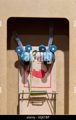 Two cute decorative blue wooden mice placed inside a classic wooden mousetrap trap in a cardboard box. Stock Photo